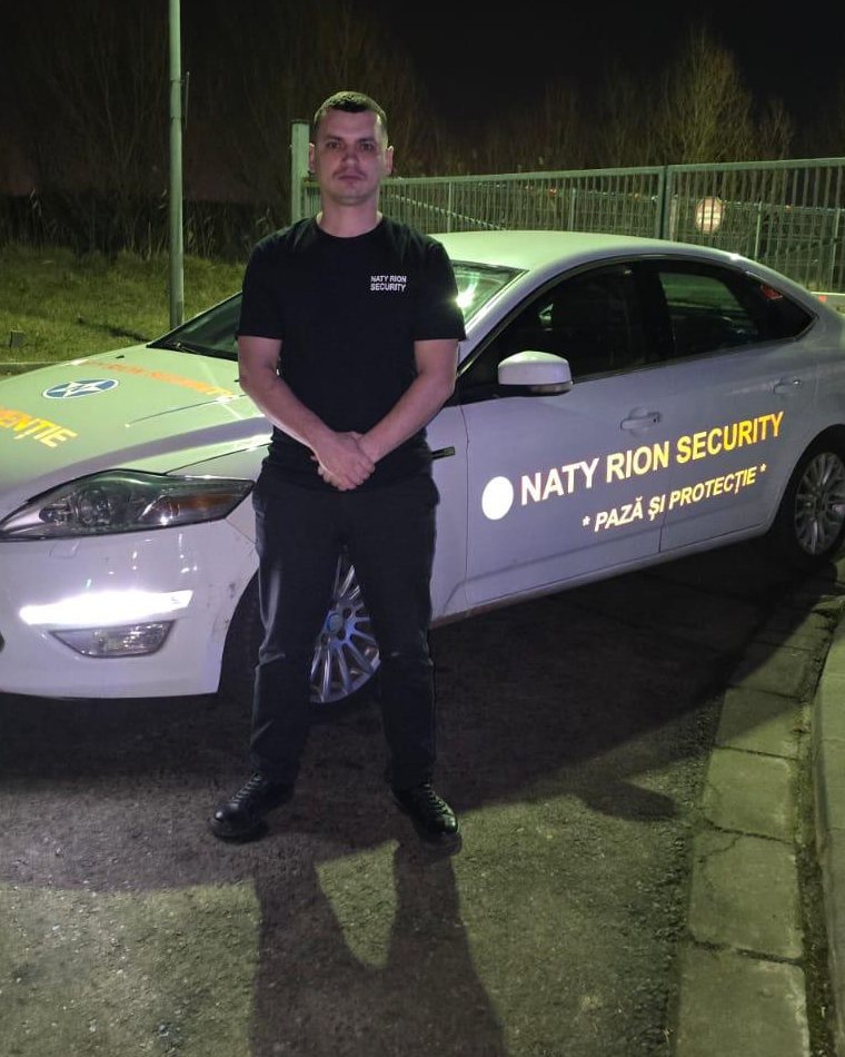 Agent NATY RION SECURITY lângă autovehiculul de intervenție, noaptea